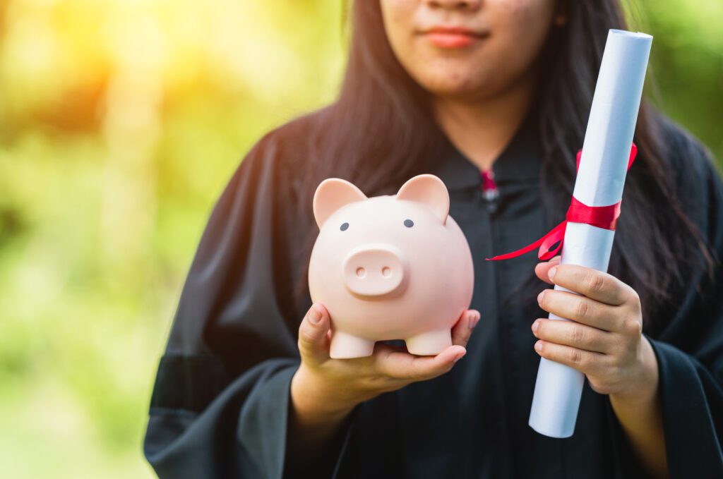 Graduate holding a diploma and piggy bank